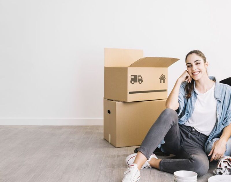 Smiling young couple sitting on the floor among packed cardboard boxes in their new home