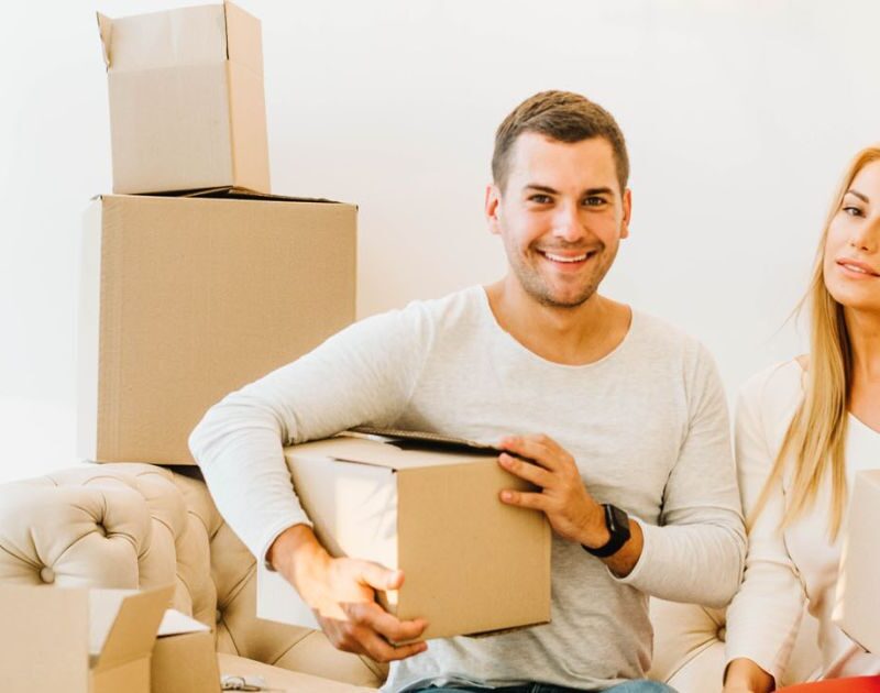 Happy couple holding packed moving boxes sitting on couch during house relocation in Dubai