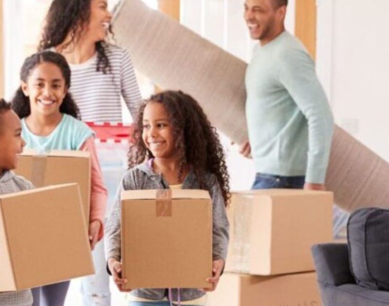 Happy family carrying cardboard boxes and rolled rug into their new living room during home move in Dubai