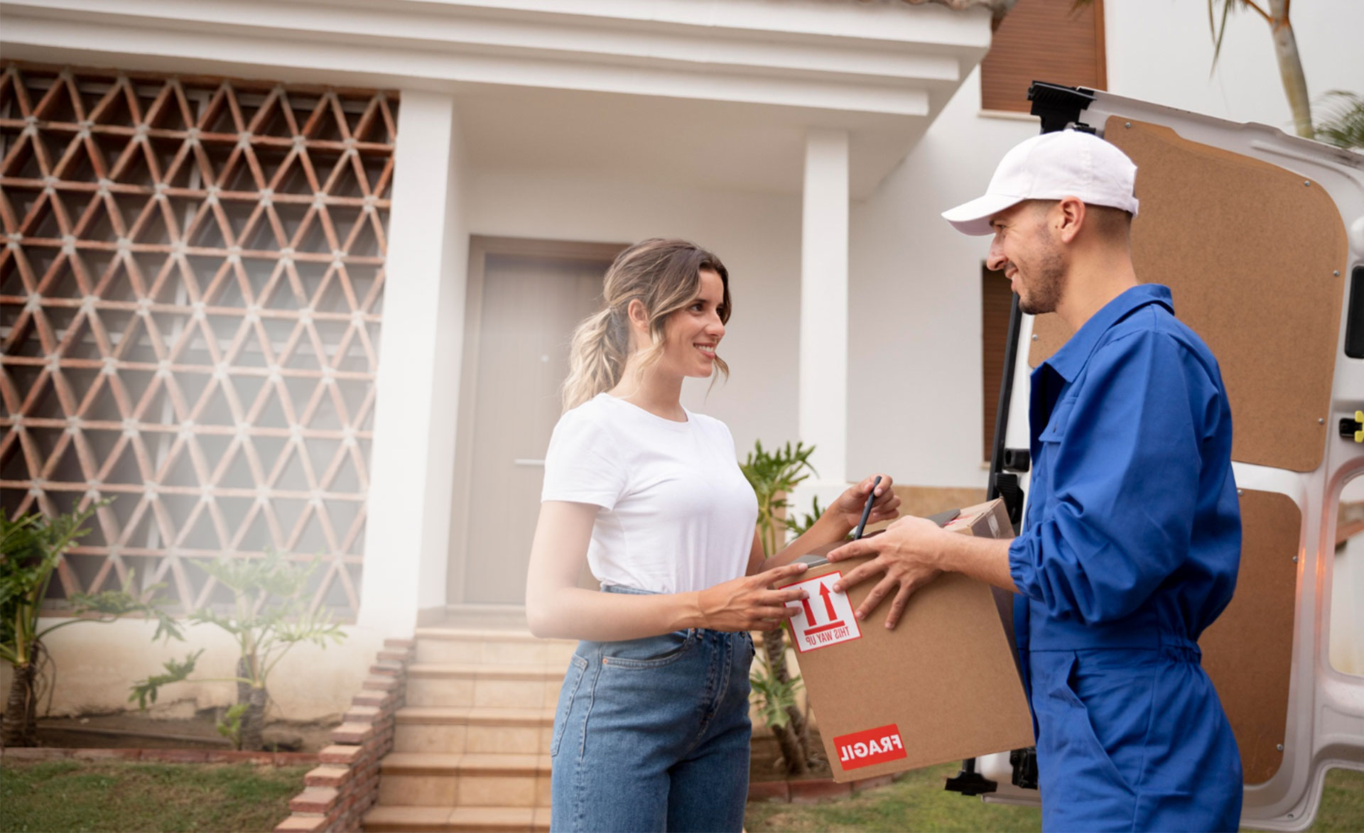 Delivery worker handing a cardboard box package to a customer outside a house in Dubai